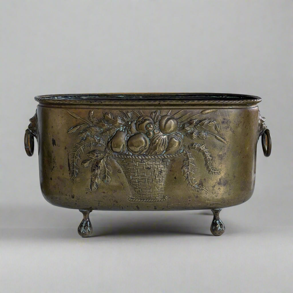 Bronze planter with decorative fruit basket design on a white surface